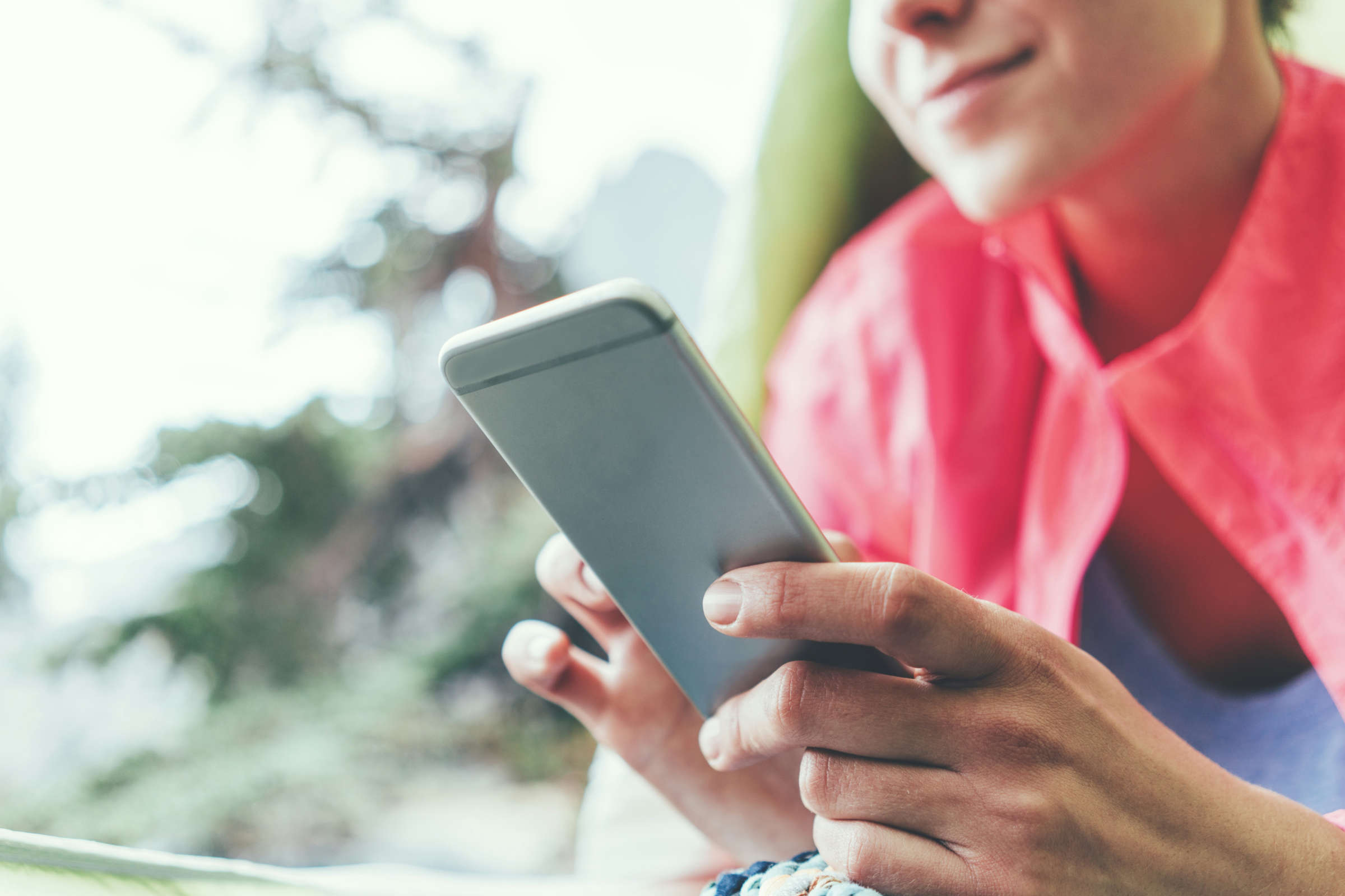 junge Frau mit roter Facke in der Natur mit Smartphone in der Hand